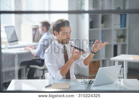 Mobile elegant businessman recording voice message on smartphone