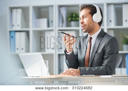 Young man in headphones and elegant suit speaking in smartphone