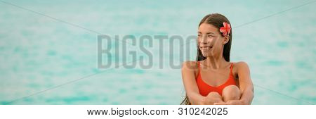 Beautiful young Asian woman natural beauty wellness spa on blue ocean water background panoramic. Happy girl smiling to the side with red flower in hair. Spa, skincare, healthy lifestyle.