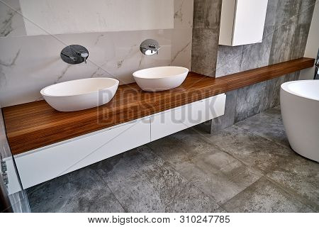 Luxury bathroom vanity. Ceramic round sinks placed on teak tabletop in luxury bathroom with gray and white marble walls