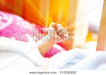 Hand Of An Energetic Newborn Baby With Light Blue And Pink Blanket And Baby Bed. Close Up.
