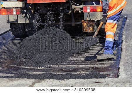 The Road Service Worker Shovel New Asphalt During Construction And Patching Of The Road.