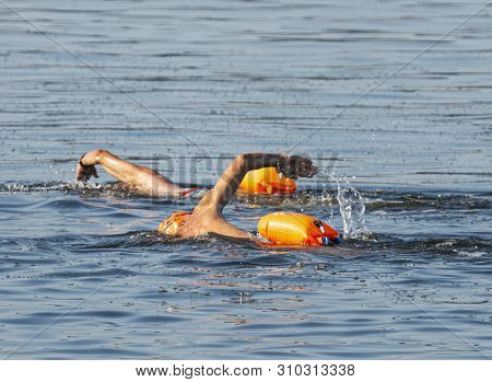 Two Male Swimmers Are Swimming In A Bay Of Water Training For A Triathlon Wearing Orange Safety Flot