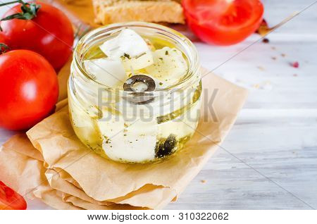 Glass Jar With Tasty Feta Cheese In Olive Oil With Olives, Spice And Pepper On Table, With Tomatoes,