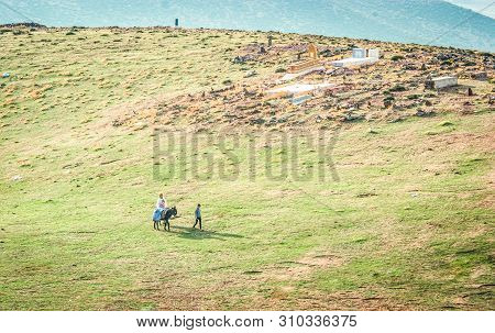 Ben Smim, Morocco - October 04, 2013. Berber Family With Donkey Passing By Small Cemetery On Meadow