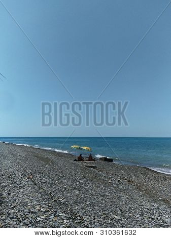 two dark silhouettes of vacationers sitting under sun umbrellas,two dark silhouettes of vacationers sitting under sun umbrellas, umbrellas yellow, pebble beach desert wild, wide strip of sky, dark blue sea