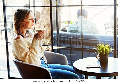 Alone Time In Coffee Shop. Young Beautiful Woman Wearing Off Shoulder Sweater Having Cup Of Hot Beve