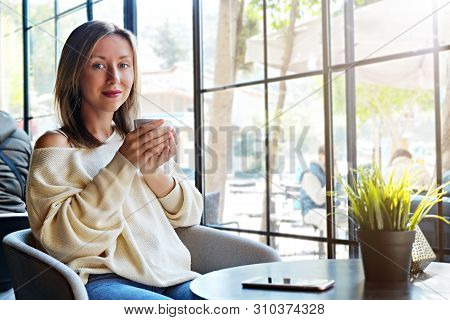 Alone Time In Coffee Shop. Young Beautiful Woman Wearing Off Shoulder Sweater Having Cup Of Hot Beve