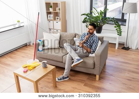 household and time management concept - indian man making to do list in notebook after home cleaning