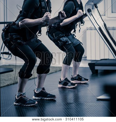 Part Of Two Fit Women In Ems Suits Doing Squatting Exercise,