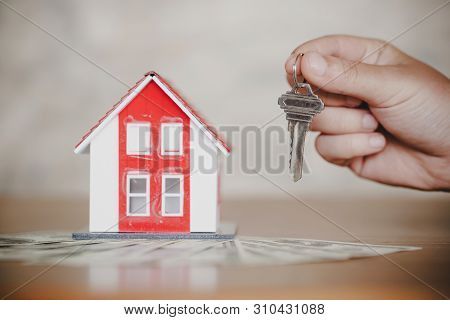 Little House Toy And One Hundred Dollar Bills On Table With A Key In Woman Hands