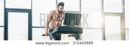 Panoramic Shot Of Handsome Sportsman With Electrodes Running On Treadmill During Endurance Test In G
