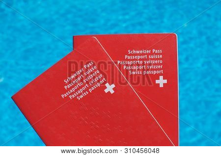 Two Swiss Passport Held In Front Of Blue Pool Water Background