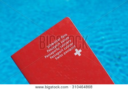 One Swiss Passport Held In Front Of Blue Pool Water Background