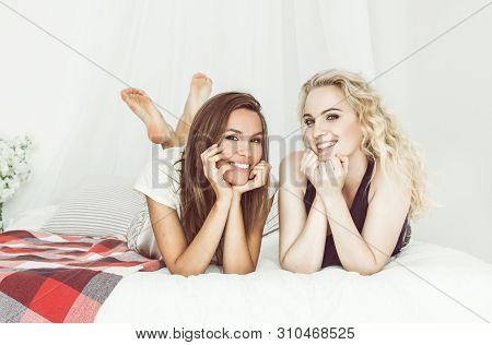 Girls' Pajamas Party. Two Women Friends Smiling While Lying On The Bed. They Are Looking At The Came