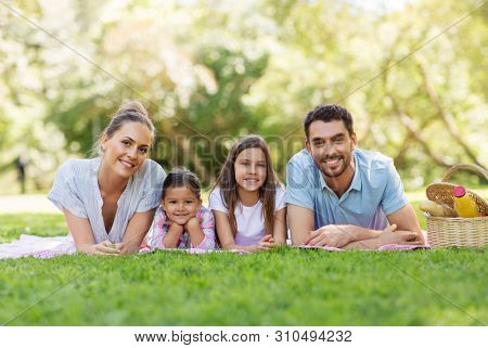 family, leisure and people concept - happy mother, father and two daughters laying on picnic blanket in summer park