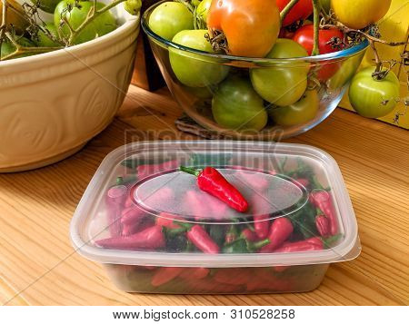 Red And Green Chilli Peppers Stored In A Plastic Container, With An Authentic Kitchen Worktop Backgr