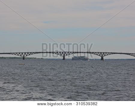 Three-deck Cruise Ship Sails Under A Large Beautiful Automobile Bridge On A Wide Blue River On A Cle