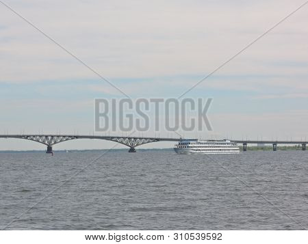 Three-deck Cruise Ship Sails Under A Large Beautiful Automobile Bridge On A Wide Blue River On A Cle