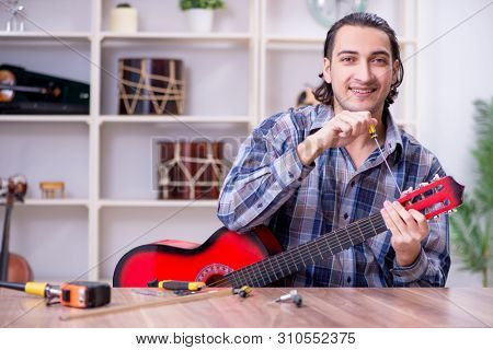 Young handsome repairman repairing guitar