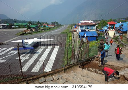 Lukla, Nepal - May 8, 2019: Nepali workers paving walkway next to fence of TenzingâHillary airport in Himalayas mountains