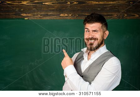 Back To School. Student In Classroom Near Blackboard Pointing At Copy Space. Male Teacher In Classro