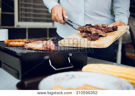 Asian Men Are Pinching Pork On A Wooden Cutting Board And Holding It To Friends Who Are Celebrating