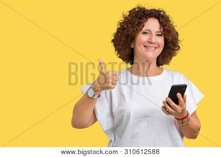 Middle ager senior woman using and texting with smartphone over isolated background happy with big smile doing ok sign, thumb up with fingers, excellent sign