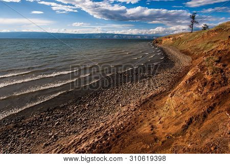 Baikal Lakeside With Mountains In The Background And Beautiful Clouds And Light. Stones By The Lake.
