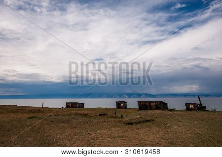 Wooden Old Sheds On The Shores Of Lake Baikal. On The Horizon Of The Mountain And It Rains. In The S