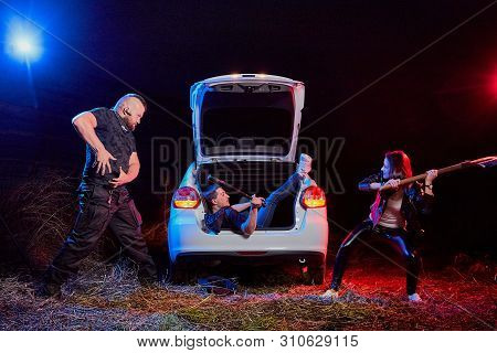 Couple Of Thugs Near Car Trying To Kill Young Guy In The Trunk At Night. Photoshoot About Life Of Gu