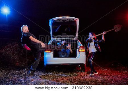 Couple Of Thugs Near Car Trying To Kill Young Guy In The Trunk At Night. Photoshoot About Life Of Gu