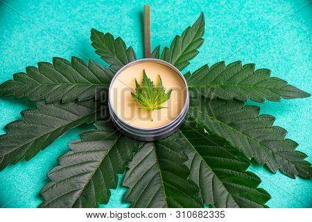 Cannabis salve with hemp and CBD oil and marijuana leaves on green background
