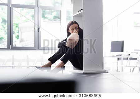 Selective Focus Of Young Lecturer Sitting On Floor And Hiding Behind Podium Tribune, While Suffering