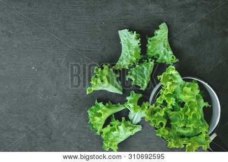 Green Lettuce Leaves In Kitchen Ladle On Stone Cutting Board On Kitchen Table.