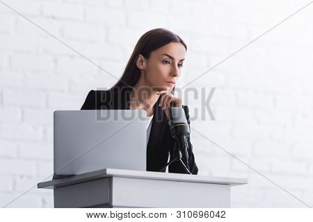 Pensive Lecturer Standing On Podium Tribune Near Microphone And Laptop