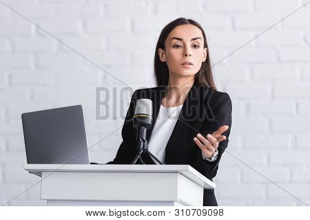Attractive Serious Lecturer Gesturing While Speaking From Podium Tribune