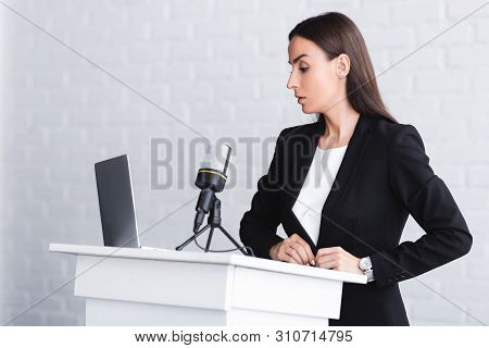 Serious Lecturer Standing On Podium Tribune Near Microphone And Laptop
