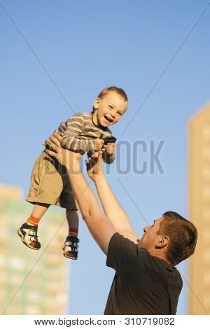 Father And Happy Son Playing Together Outdoors.dad Tossing Son Up Against Blue Sky.  Vertcal Image
