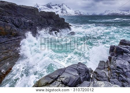 Roaring Ocean Near Rocky Shore Of Picturesque Lofoten Islands Against Snowy Mountains In Norway At S