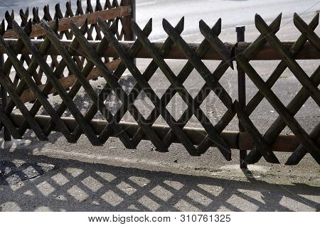 Trellis-work Fence At Courtyard Entrance Casting Shadow On Tarmac On Sunny Day