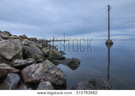 Stone Coastline Of The Island Of Grotta Near Reykjavik With Clouds In The Sky. Lighthouse And Uninha