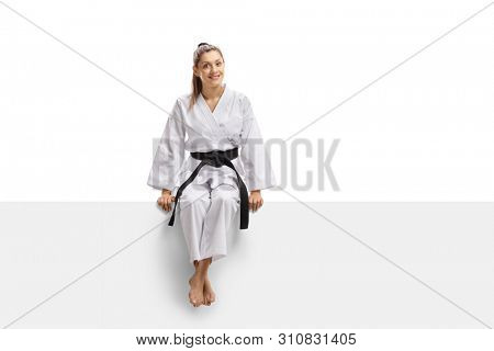 Full length portrait of a young woman in kimono and black belt sitting on a banner isolated on white background