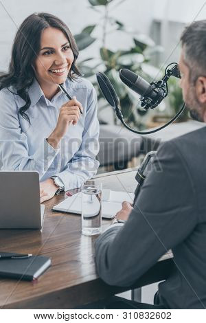 Cheerful Radio Host Looking At Businessman During Interview In Broadcasting Studio