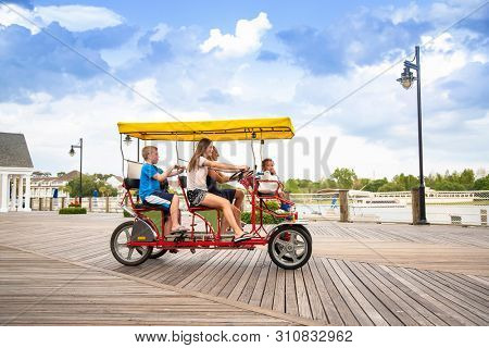 Young happy family riding a double surrey tandem bicycle on a large ocean boardwalk. Outdoor summer fun with kids