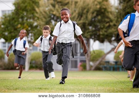 Excited Elementary School Pupils Wearing Uniform Running Across Field At Break Time