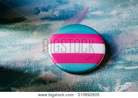 closeup of a badge patterned with a transgender pride flag on a surface painted with brushstrokes of different colors
