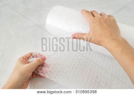 Woman Hands Holdind A Roll Of White Transparent Bubble Wrap On A Rough White Background. Material Fo