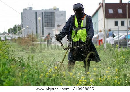A Man In A Protective Suit Mows The Grass With A Handheld Portable Lawnmower. Improvement And Econom