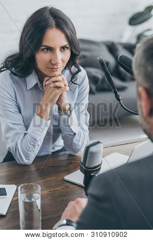 Selective Focus Of Attractive Radio Host Sitting With Clenched Hands During Interview With Businessm